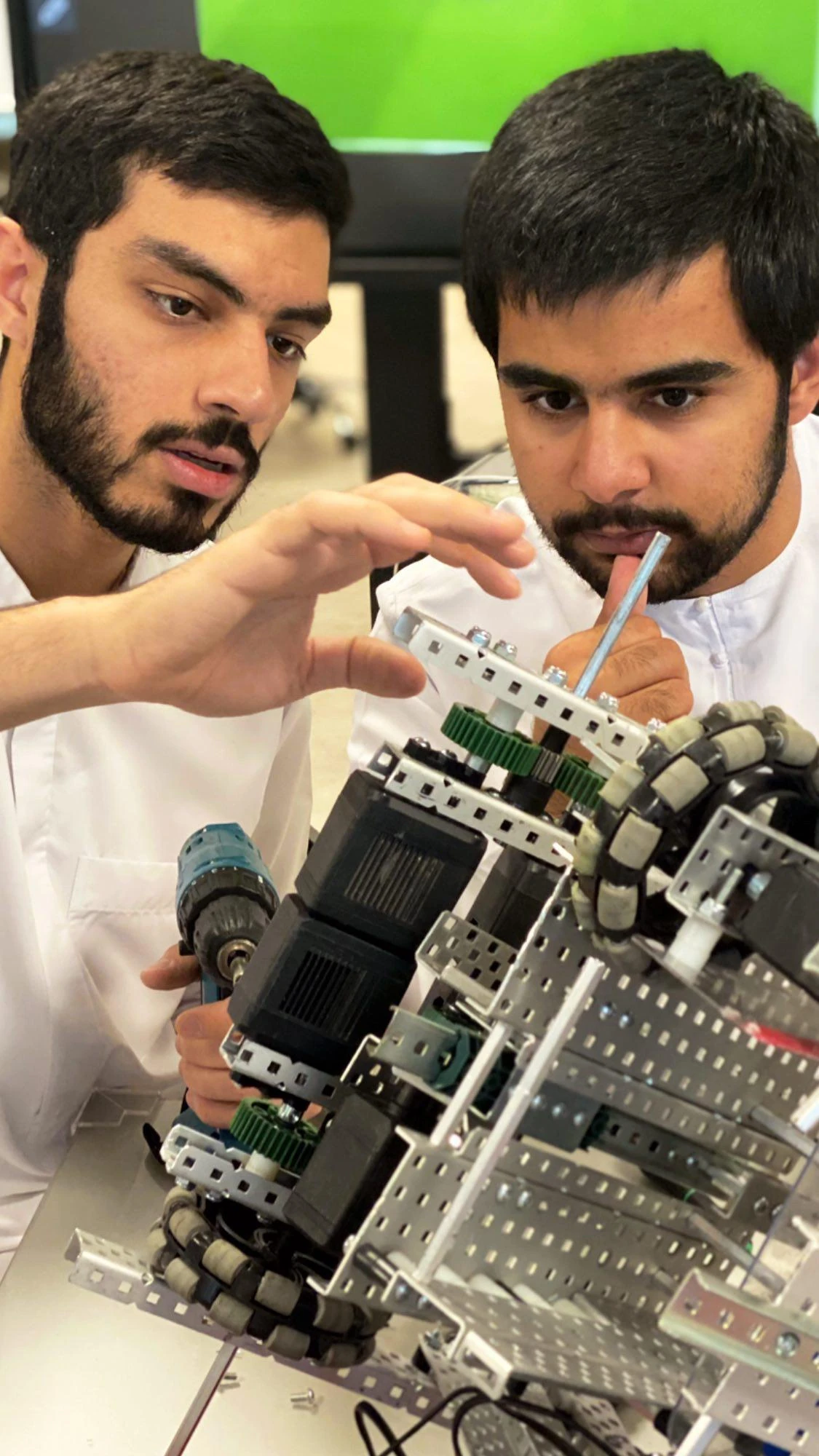 Two people adjusting the gears and frame of a robot assembly